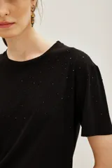 Remera negra de manga corta con cuello redondo, decorada con pequeñas aplicaciones brillantes dispersas en la parte frontal y mangas.