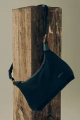 Bandolera estilo hobo de cuero color negro, con correa ajustable y detalles metálicos dorados. Presenta el logo de la marca grabado en el frente.