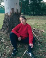 Sweater unisex de lana merino fina color rojo, con cuello redondo y corte relajado. Presenta un motivo inspirado en la técnica de zurcido visible.