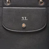 Cartera estructurada mediana de material símil cuero negro, con doble manija fija y correa larga regulable y desmontable. Presenta solapa frontal con botón imantado y herrajes metálicos plateados.