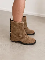 Bota corta de cuero gamuzado color marrón, con diseño de polaina superpuesta y detalle de hebillas metálicas en la parte posterior del talón. Cuenta con suela plana de goma negra y horma amplia.