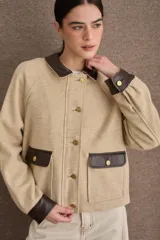 Campera corta de paño color marrón con detalles en cuero sintético al tono en cuello, puños y solapas de bolsillos. Presenta cierre frontal con botones metálicos dorados y dos bolsillos frontales tipo cargo.