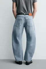 Jeans de denim de algodón en color negro con efecto lavado, corte amplio y silueta curva tipo barrel fit con pinzas en las rodillas. Presenta diseño clásico de cinco bolsillos y cierre frontal con cremallera y botón metálico.