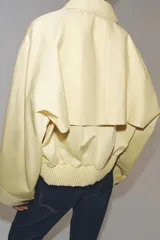 Chaqueta corta confeccionada en mezcla de algodón color amarillo claro, con cuello de solapa, manga larga, bolsillos delanteros y cierre frontal con botones visibles en los extremos.