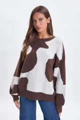 Buzo de punto con diseño jacquard de manchas abstractas en tonos marrón y crema, de corte holgado, cuello redondo y mangas largas con puños ajustados.
