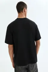 Remera negra de punto de algodón de peso medio, cuello redondo ribeteado y hombros caídos con corte relajado.