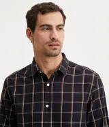 Camisa de hombre de manga larga, confeccionada en franela ligera con estampado cuadrillé en tonos oscuros y líneas finas blancas y naranjas. Cuenta con cuello clásico y abotonado frontal.
