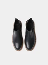 Botin de mujer de cuero negro, estilo chelsea, con elásticos laterales, tirador trasero y suela dentada de goma color caramelo.