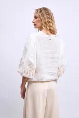 Blusa blanca de lino con cuello mao, mangas 3/4 abullonadas con apliques bordados en forma de hojas y cierre frontal con botones.