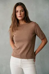 Sweater de tejido de punto fino en color arena, con cuello redondo y mangas cortas. Presenta un diseño minimalista con un pequeño detalle metálico en el ruedo.