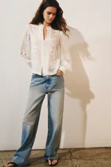 Camisa de organza de viscosa color crudo, con cuello subido, escote en V y manga larga. Presenta detalles de bordados florales en contraste a lo largo del frente y cierre frontal con botones.