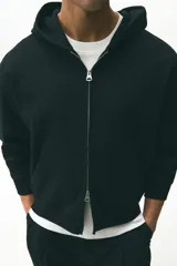 Campera con capucha de felpa pesada, con cierre frontal, bolsillos laterales y puños y bajo acanalados. Presenta un corte holgado y diseño minimalista.