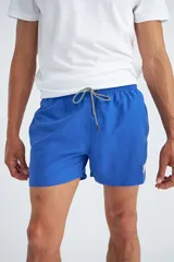 Short de baño de corte clásico, color azul, con cintura elástica y cordón ajustable bicolor. Cuenta con un pequeño parche decorativo en el lateral.