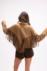 Chaqueta de efecto gamuza en color tostado, con solapas amplias, cierre frontal con un botón y flecos largos decorativos en la parte frontal y trasera de las mangas. Presenta una estructura definida y forro interior.