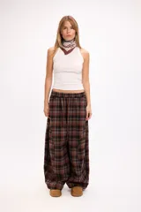 Pantalon de corte oversize y tiro medio, confeccionado en tela con estampado de cuadros en tonos marrones y negros. Presenta una silueta amplia y holgada con cintura elástica y cordón ajustable.