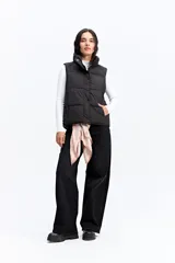 Chaleco puffer negro con cuello alto, cierre frontal y broches a presión. Diseño acolchado liviano con bolsillos laterales.