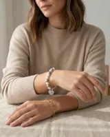 Pulsera elástica compuesta por una combinación de perlas blancas y esferas metálicas plateadas, con un dije colgante en forma de corazón con grabado.