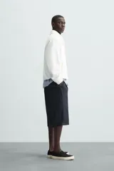 Cazadora tipo canguro de calce relajado, color blanco roto o crema, confeccionada en mezcla de lyocell y algodón. Presenta cuello solapa con cierre frontal de botonadura oculta, manga larga con puños elásticos y bolsillos frontales de vivo. El bajo es ajustable con elástico oculto en los laterales.