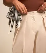 Pantalón carrot color beige confeccionado en tricolina con efecto empapelado, cierre tradicional y pliegues.