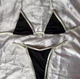 Conjunto de bikini clásico en color negro con ribetes y tiras en tono blanco. Consta de un corpiño triangular con tiras regulables para el cuello y la espalda, y una bombacha colaless con tiras laterales ajustables.