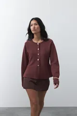 Cardigan de punto color bordó, con cuello redondo, manga larga y cierre frontal con botones metálicos. Presenta un diseño entallado en la cintura con una silueta levemente evasé.