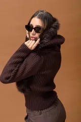 Campera corta de diseño combinado en color marrón. Presenta cuerpo de piel sintética con capucha, mangas tejidas en punto acanalado y cierre frontal con vista de cuero sintético. Incluye detalles de pompones laterales en el ruedo.