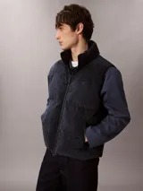 Chaleco acolchado reversible Calvin Klein, con diseño sin mangas, cuello alto y cierre frontal de cremallera. Presenta un lado de pana y otro de nailon liso.