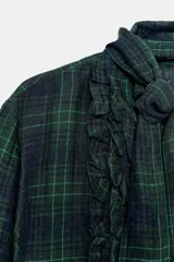 Blusa de manga larga con estampado de cuadros escoceses en tonos verde oscuro y azul marino. Presenta cuello redondo con un pañuelo incorporado que se anuda, y volantes verticales en el frente.