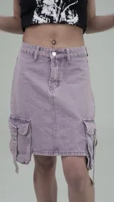 Pollera de jean estilo cargo en color violeta, con corte recto y tiro medio. Presenta bolsillos laterales tipo cargo con solapas y hebillas metálicas decorativas, además de bolsillos frontales y traseros clásicos.