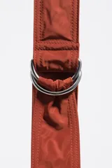 Bolso tipo hobo de la marca Bimba y Lola, modelo Moon mediano, de color rojo óxido. Confeccionado en nylon con diseño de media luna, cierre superior con cremallera, correa ajustable con hebilla metálica y el logotipo de la marca impreso en la parte frontal.