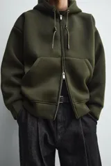 Sudadera de corte relajado confeccionada en tejido técnico con elasticidad y efecto neopreno. Presenta capucha ajustable con cordones, cierre frontal de cremallera de doble dirección, bolsillos tipo canguro y terminaciones en rib.