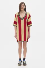 Vestido corto tejido calado a rayas horizontales rojas y amarillas, con cuello en V y detalle de botón azul.
