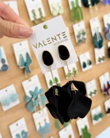 Caravanas colgantes con diseño de pétalos negros en la parte inferior, unidos a una pieza superior ovalada de color negro con borde dorado mediante una varilla metálica dorada.