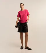 Blusa fucsia de manga corta con cuello redondo pespunteado, diseño sin estampa y efecto airflow con textura sutil. Cuenta con abertura trasera tipo gota y cierre con botón.