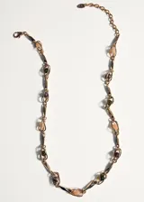 Collar dorado de cadena eslabonada con inserciones de eslabones metálicos entrelazados y detalles de piedras en tonos rosa, marrón y verde.