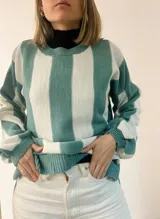 Sweater de punto con diseño de rayas verticales en tonos azul y gris, con sutil acabado brillante. Presenta cuello redondo, mangas largas con puños ajustados y corte amplio con aberturas laterales en el ruedo.