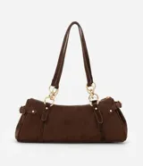 Cartera mediana de diseño alargado y estructura firme, confeccionada en gamuza sintética de color marrón. Cuenta con doble asa fina sujeta por argollas metálicas doradas, cierre superior y detalles de solapas decorativas con tachas en los laterales.