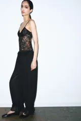 Body de encaje negro con diseño de corsetería, escote en pico y tirantes finos ajustables. Presenta paneles de encaje floral con transparencias y costuras estructuradas.