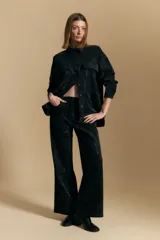 Pantalón de corte recto y silueta amplia, confeccionado en tejido de textura aterciopelada color negro. Presenta un diseño de tiro alto con costuras verticales decorativas en el frente y bolsillos laterales.