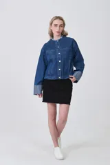 Campera corta de denim azul oscuro, con cuello mao deshilachado y botones plateados frontales. Las mangas largas tienen puños anchos con estampado de rayas verticales en tonos celestes y blancos.