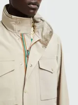 Chaqueta Moncler de estilo utilitario en color beige, con cuello alto, cierre frontal con botones a presión y múltiples bolsillos delanteros.