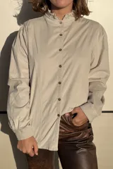 Camisa de pana color verde oliva, con cuello alto con volados, cierre frontal de botones y mangas largas con puños.