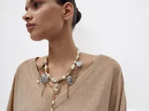 Collar de diseño maximalista compuesto por una cadena de perlas y esferas metálicas doradas, adornado con múltiples dijes colgantes que incluyen medallas grabadas, un camafeo central, corazones y cadenas finas plateadas y doradas.