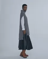 Chaleco largo de punto trenzado color gris con cuello alto y cierre frontal con cremallera metálica.