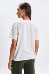 Remera de manga corta color crudo con estampa frontal rectangular en tonos marrones y dorados con diseño floral y la frase 'Grow as you go'.