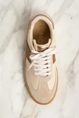 Zapatillas bajas color crema con puntera de gamuza beige, detalle de franja lateral en cuero marrón y contrafuerte en cuero metalizado color cobre.