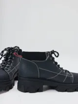 Bota acordonada de estilo montañés con suela track de goma robusta. Confeccionada en cuero con detalles de gamuza en la talonera y tirador trasero. Presenta costuras a contratono y cordones bicolores.