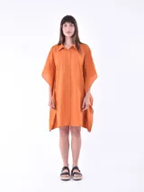 Vestido camisero naranja de manga corta tipo murciélago, con cuello polo y cierre frontal de botones. El ruedo es asimétrico con aberturas laterales.