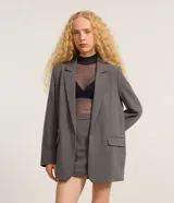 Blazer gris de sastrería, corte oversized, con cuello con solapas, manga larga y bolsillos frontales.