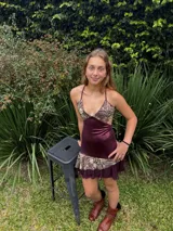 Vestido corto de tela metalizada en tono fucsia con reflejos dorados, con escote en V, diseño de top con triángulos, aberturas laterales en la cintura y doble volado irregular en el ruedo.
